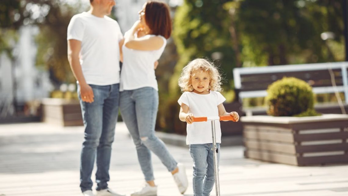 Happy family with child on scooter in sunny park, enjoying outdoor time together.
