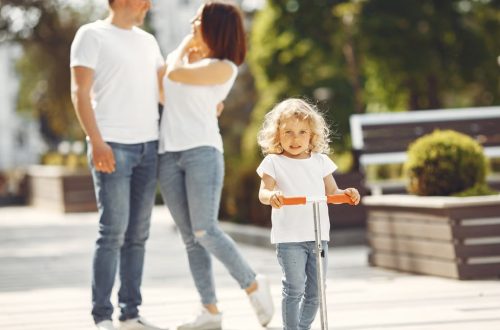 Happy family with child on scooter in sunny park, enjoying outdoor time together.